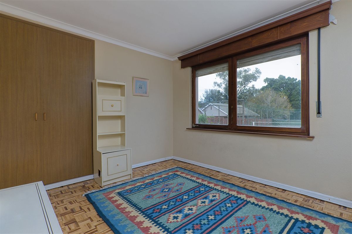 A vacant bedroom featuring original parquet flooring, a built-in wardrobe, and timber-framed windows, offering a blank canvas for renovation and modernization.