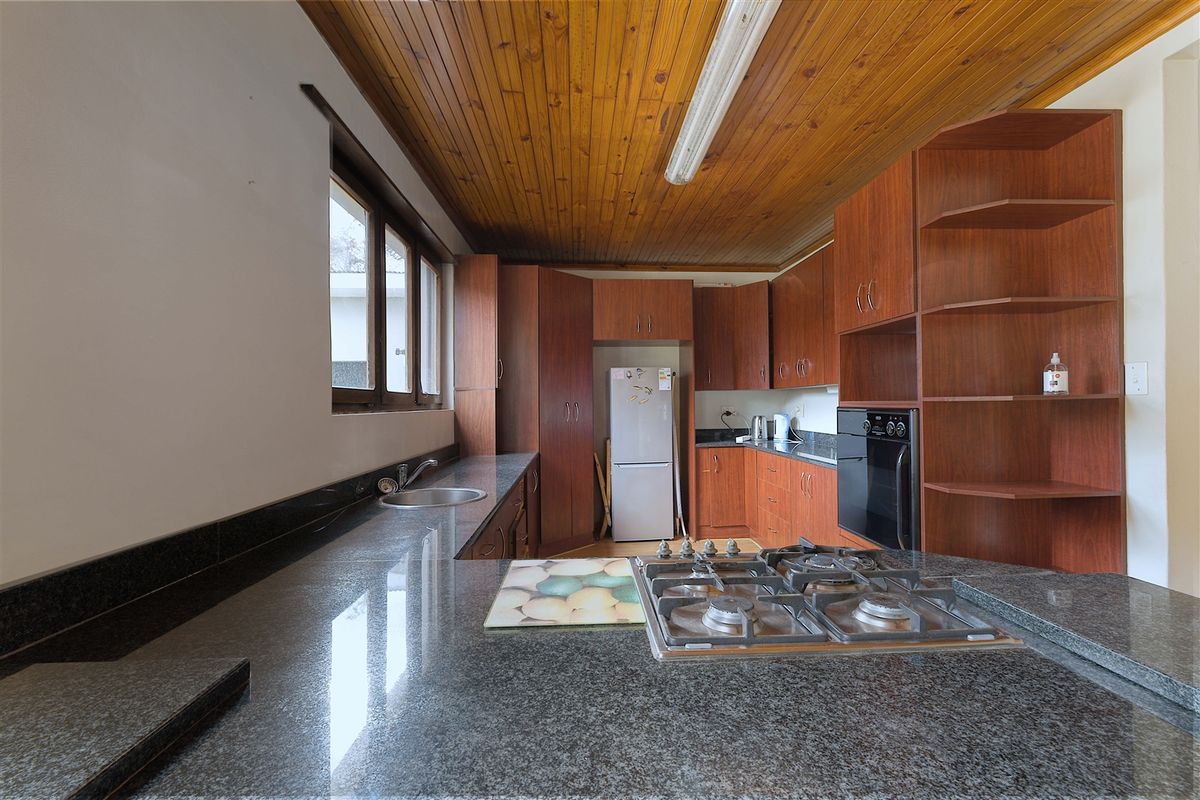 A functional kitchen featuring granite countertops, a gas hob, built-in oven, and warm timber ceiling finishes with ample storage cabinetry.
