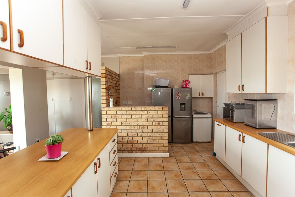A functional kitchen featuring laminate countertops, ample built-in cabinetry, and a distinctive exposed brick wall, finished with ceramic floor tiles.