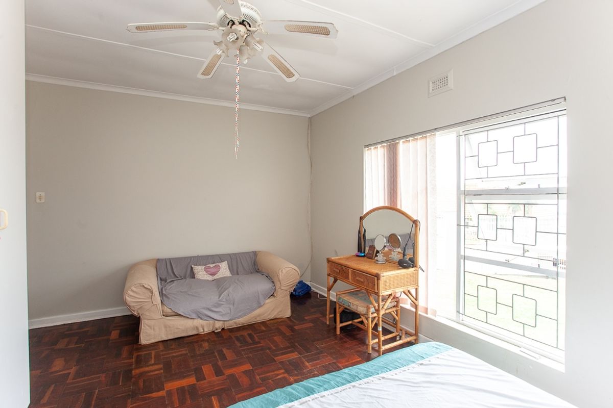 A bedroom featuring classic parquet flooring, a ceiling fan, and a window fitted with a decorative security gate.