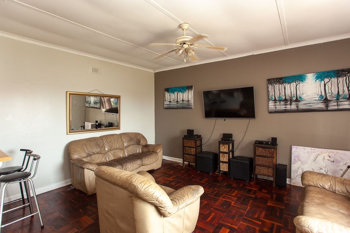 A living room featuring dark parquet flooring, a ceiling fan, and a neutral color palette with a dark accent wall.