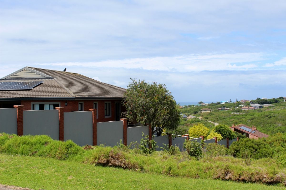 Rear view of a residential property featuring a tiled roof with solar panels and a secure brick and concrete boundary wall overlooking the landscape.