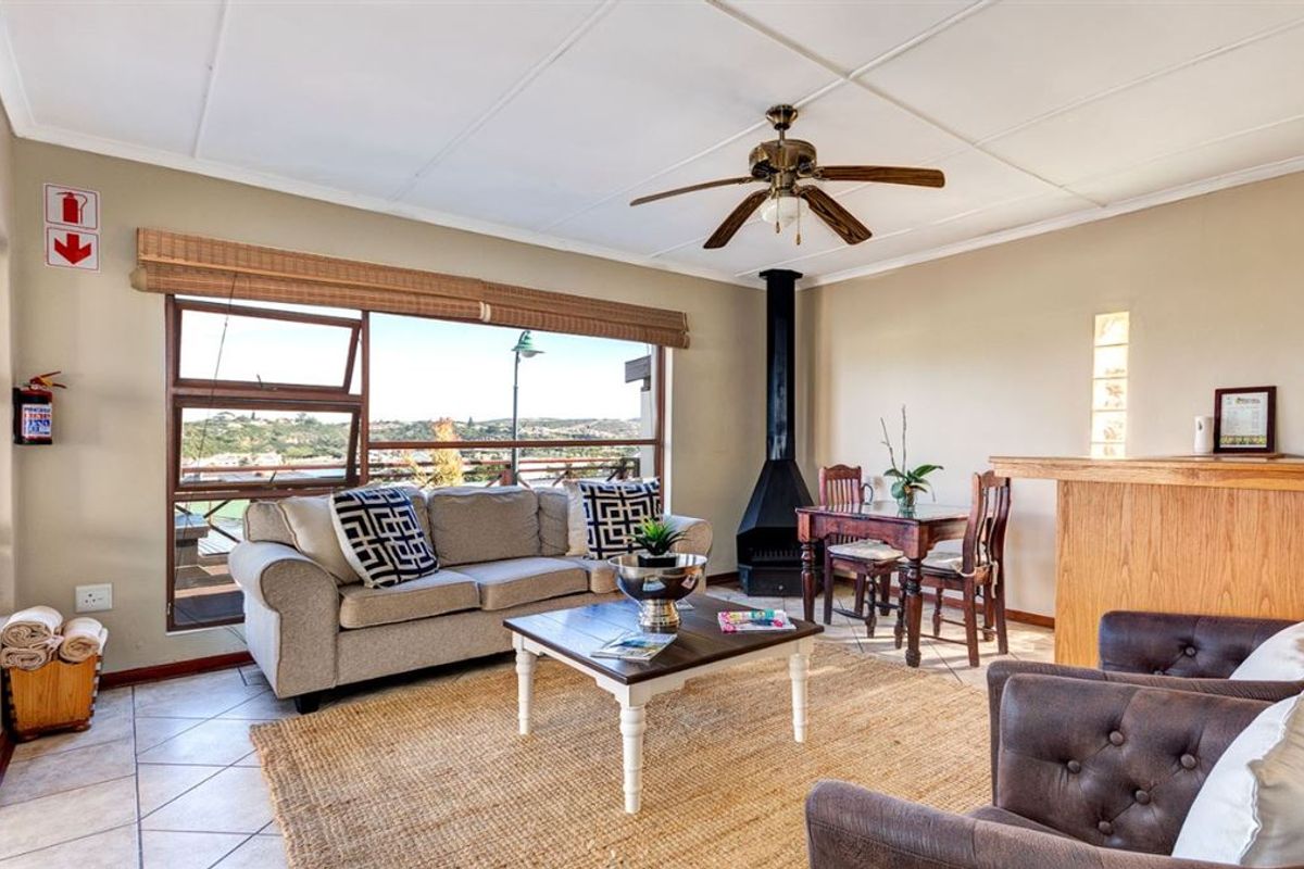 A comfortable living area featuring a freestanding fireplace, ceiling fan, tiled floors, and a built-in bar counter with views through a large window.