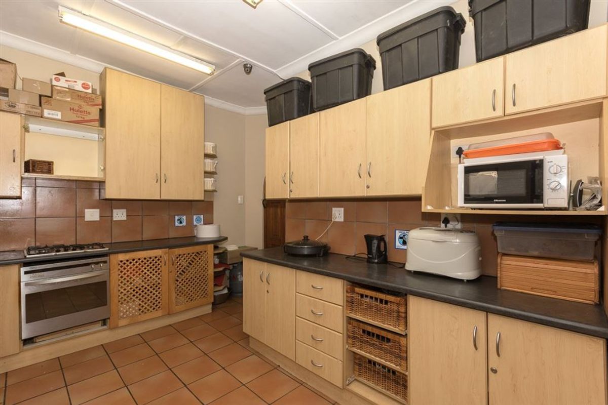 A functional kitchen featuring light wood cabinetry, dark laminate countertops, gas stove, and tiled flooring with a practical layout.