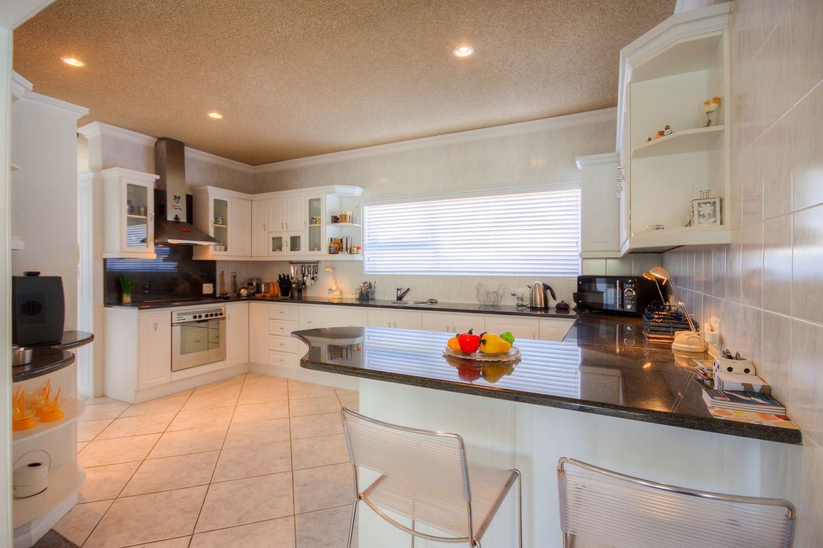 A well-maintained kitchen featuring white cabinetry, dark granite countertops, tiled flooring, and integrated appliances with recessed ceiling lighting.
