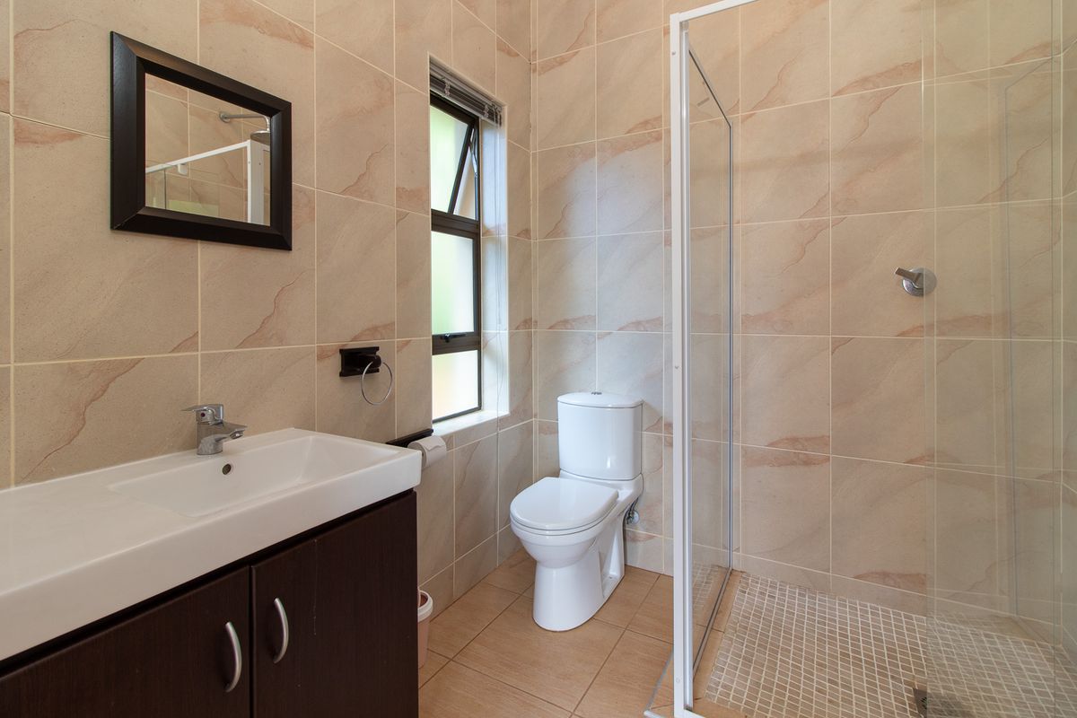 A clean, functional bathroom featuring a vanity cabinet, toilet, and a glass-enclosed shower with neutral wall and floor tiling.