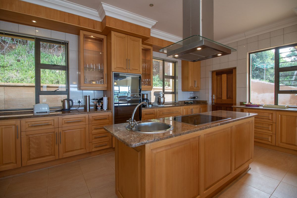 A well-maintained kitchen featuring warm wooden cabinetry, granite countertops, a central island with a hob, and a stainless steel extractor fan.