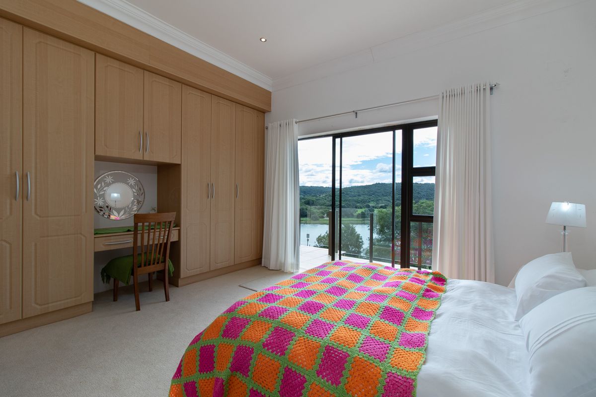 Spacious bedroom featuring extensive built-in cabinetry, neutral carpeting, and large sliding doors opening to a scenic balcony with water views.