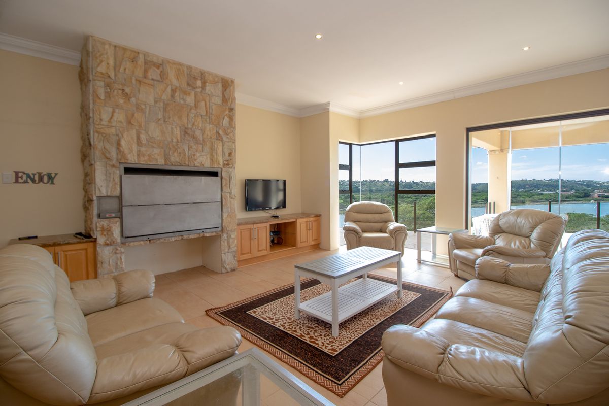 Spacious living room featuring a prominent stone-clad fireplace, built-in cabinetry, and large windows offering scenic views with access to an outdoor patio.