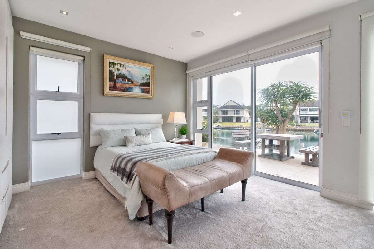 A well-maintained bedroom featuring neutral carpeting, recessed lighting, and large sliding glass doors that provide direct access to a patio with water views.