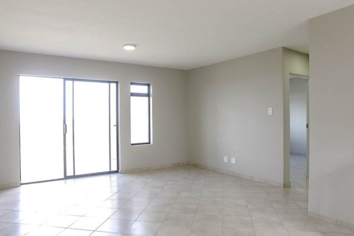 Spacious open-plan living area featuring neutral tiled flooring, sliding glass doors for natural light, and direct access to the kitchen area.