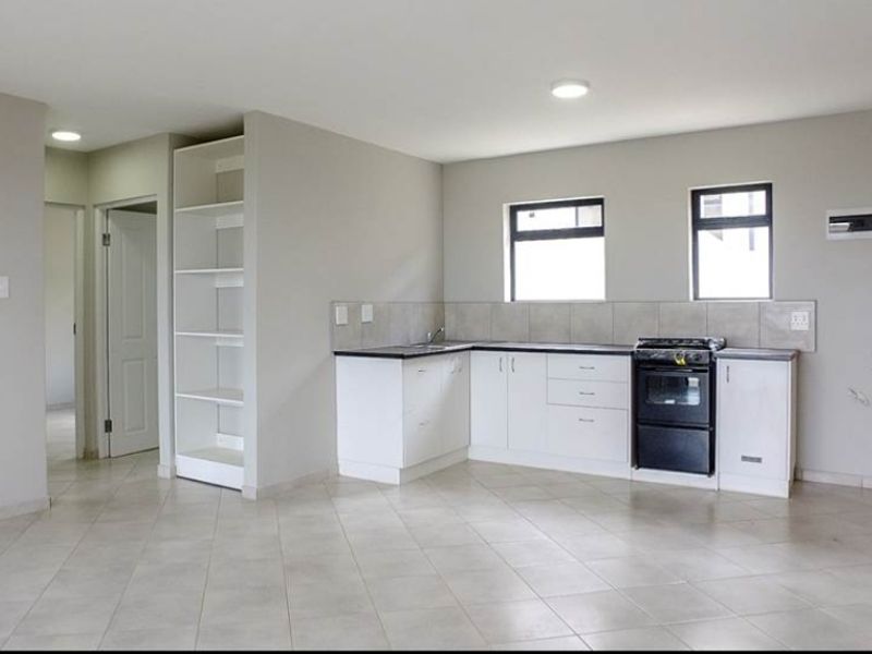 An open-plan living and kitchen area featuring neutral tiled flooring, white cabinetry, built-in shelving, and a gas stove.
