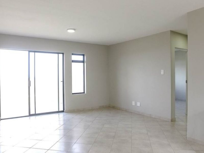 Spacious open-plan living area featuring neutral tiled flooring, sliding glass doors for natural light, and direct access to the kitchen area.