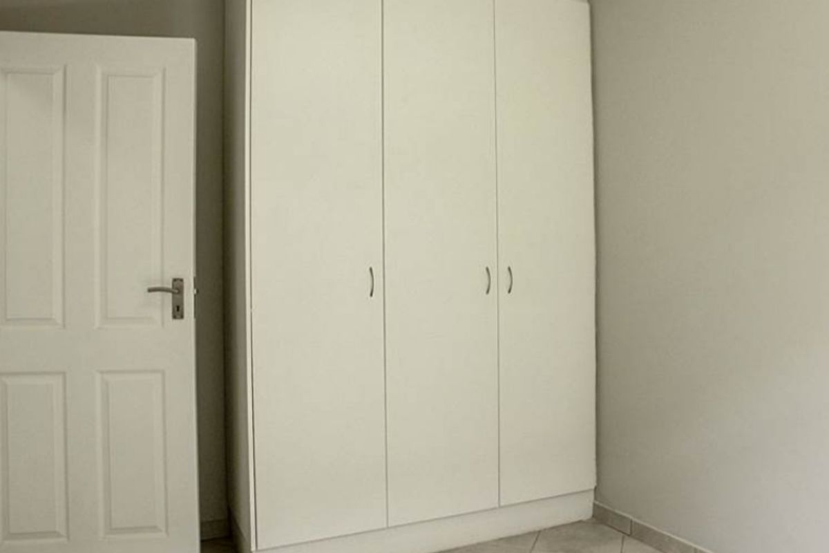A clean, empty bedroom featuring neutral tiled flooring and a white built-in wardrobe with ample storage space.