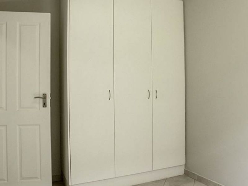 A clean, empty bedroom featuring neutral tiled flooring and a white built-in wardrobe with ample storage space.