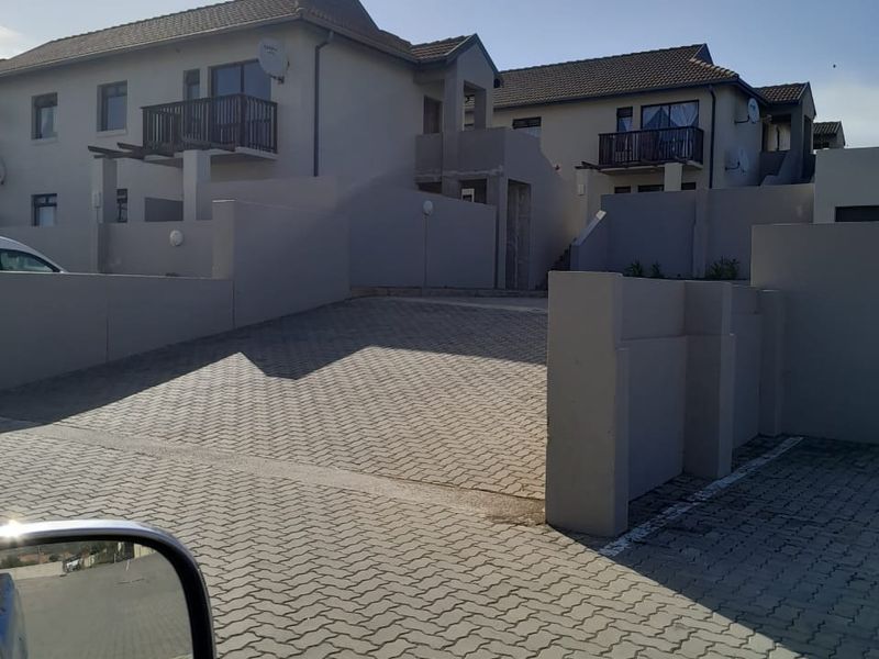 Front view of a residential flat complex featuring paved driveway access, boundary walls, and upper-level balconies.