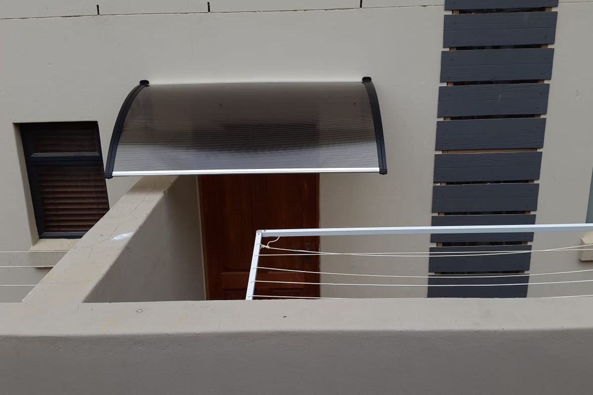 Rear exterior view of the flat featuring a timber entrance door, a protective polycarbonate awning, and a fixed wall-mounted washing line.