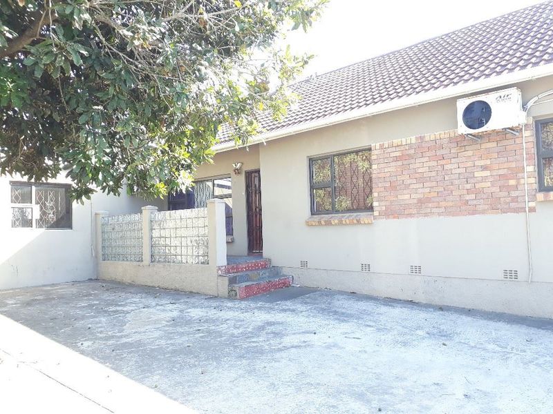 Front exterior view of the house featuring a concrete driveway, tiled roof, brick facade accents, and a decorative glass block wall.