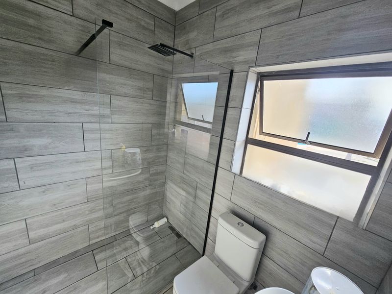Modern bathroom featuring a walk-in shower with a rain shower head, glass screen, and contemporary grey wood-look tiling throughout.