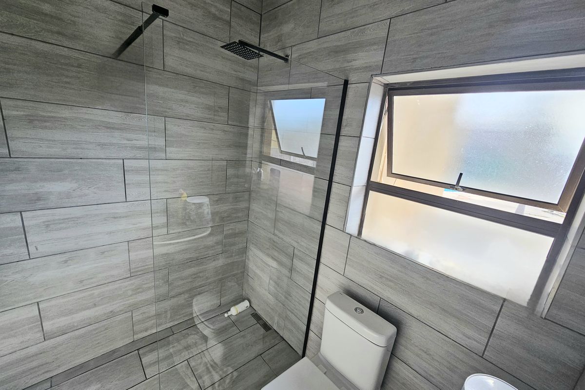 Modern bathroom featuring a walk-in shower with a rain shower head, glass screen, and contemporary grey wood-look tiling throughout.