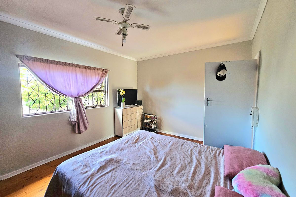 A functional bedroom featuring timber flooring, a ceiling fan, and security bars on the window, offering a neutral base for personalization.