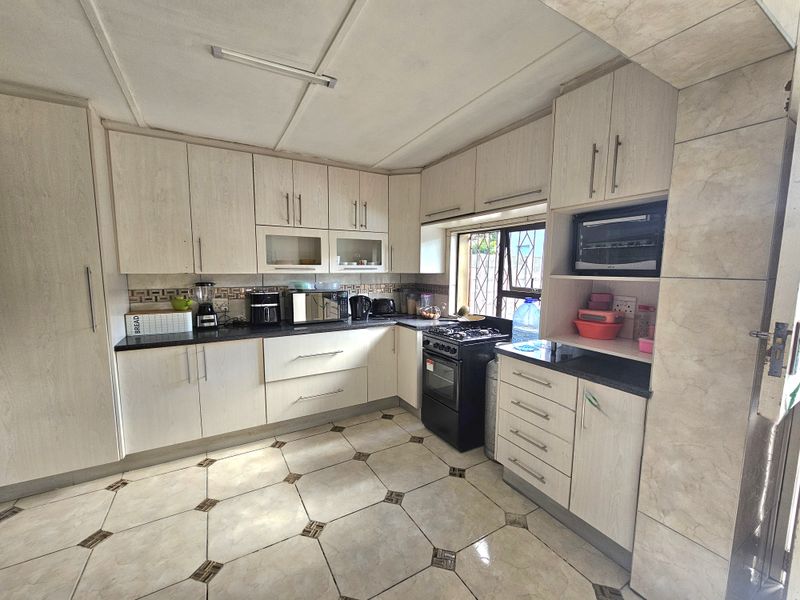 A functional kitchen featuring light-toned laminate cabinetry, granite countertops, a tiled backsplash, and a freestanding stove, offering a practical layout for daily cooking.