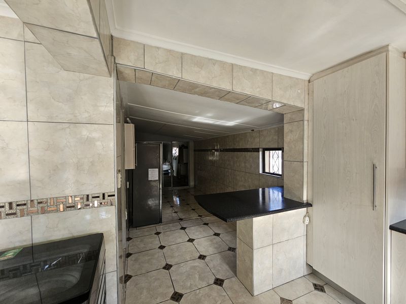 A functional kitchen area featuring tiled flooring, wall tiling, built-in cabinetry, and a breakfast bar with granite countertops.