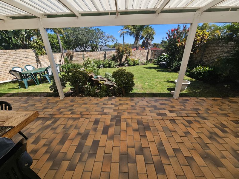 A covered patio area featuring brick paving and a pergola, overlooking a well-maintained garden with a brick boundary wall.