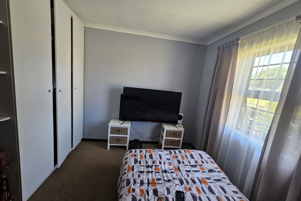 A functional bedroom featuring built-in cupboards, carpeted flooring, and natural light from a window with curtain tracks.