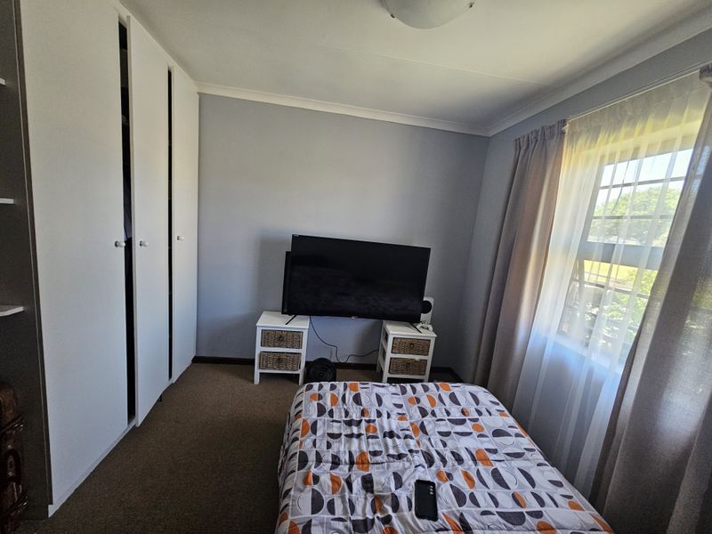 A functional bedroom featuring built-in cupboards, carpeted flooring, and natural light from a window with curtain tracks.