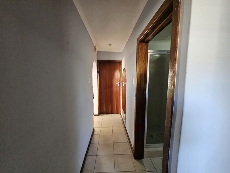 A clean, tiled hallway featuring wooden door frames and an arched transition, providing access to adjacent rooms.