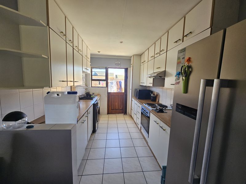 A functional galley-style kitchen featuring white built-in cabinetry, wooden countertops, tiled flooring, and integrated cooking appliances with direct access to the rear exterior.