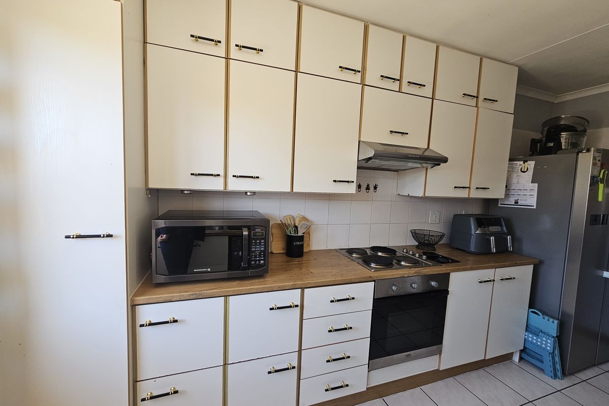 A functional kitchen featuring white cabinetry with gold-tone hardware, wood-look laminate countertops, a built-in oven, gas hob, and tiled flooring.