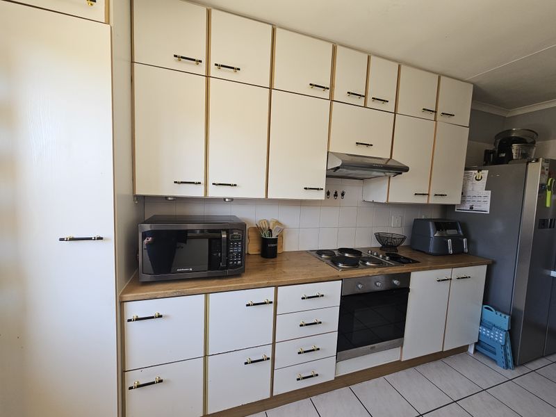 A functional kitchen featuring white cabinetry with gold-tone hardware, wood-look laminate countertops, a built-in oven, gas hob, and tiled flooring.