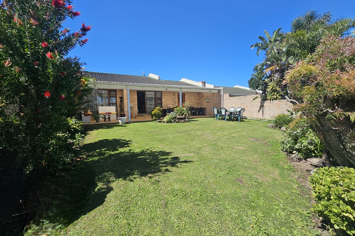 A spacious rear garden featuring a well-maintained lawn, established landscaping, and a covered patio area attached to the main house structure.