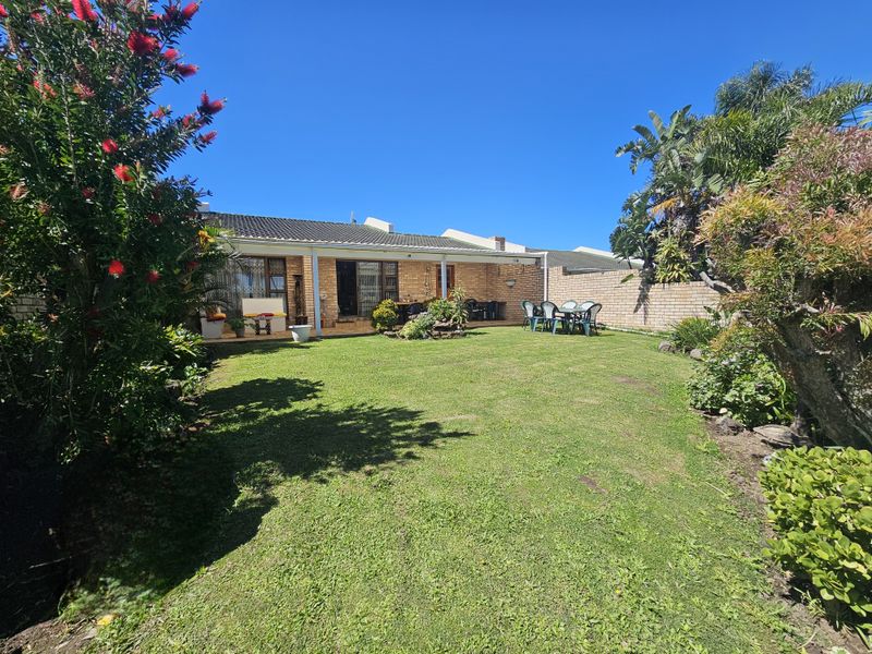 A spacious rear garden featuring a well-maintained lawn, established landscaping, and a covered patio area attached to the main house structure.
