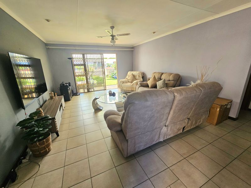 Spacious living room featuring neutral tiled flooring, a ceiling fan, and a sliding glass door providing access to the outdoor area.