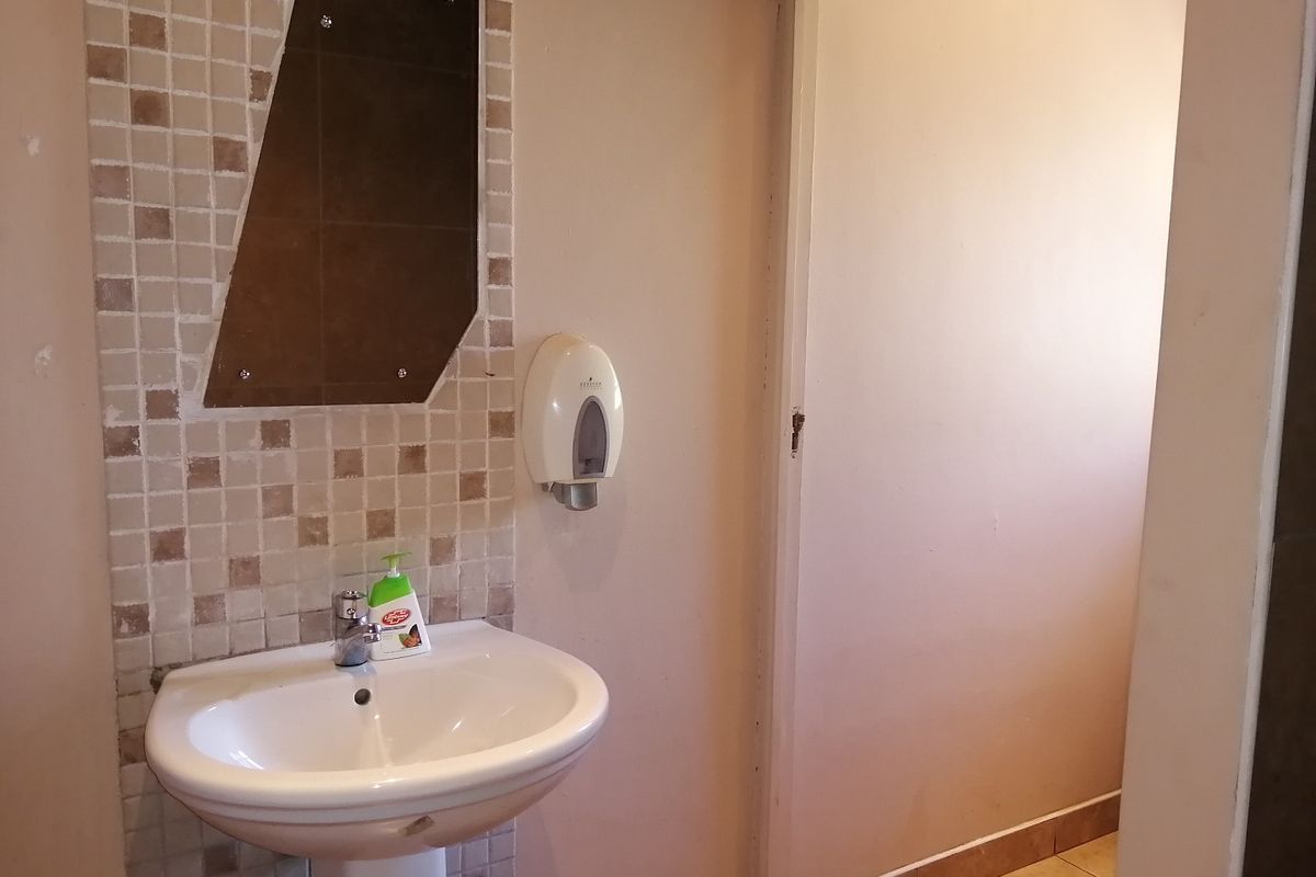 A functional bathroom featuring a pedestal basin with a tiled splashback and wall-mounted soap dispenser, requiring cosmetic updates to improve its overall condition.