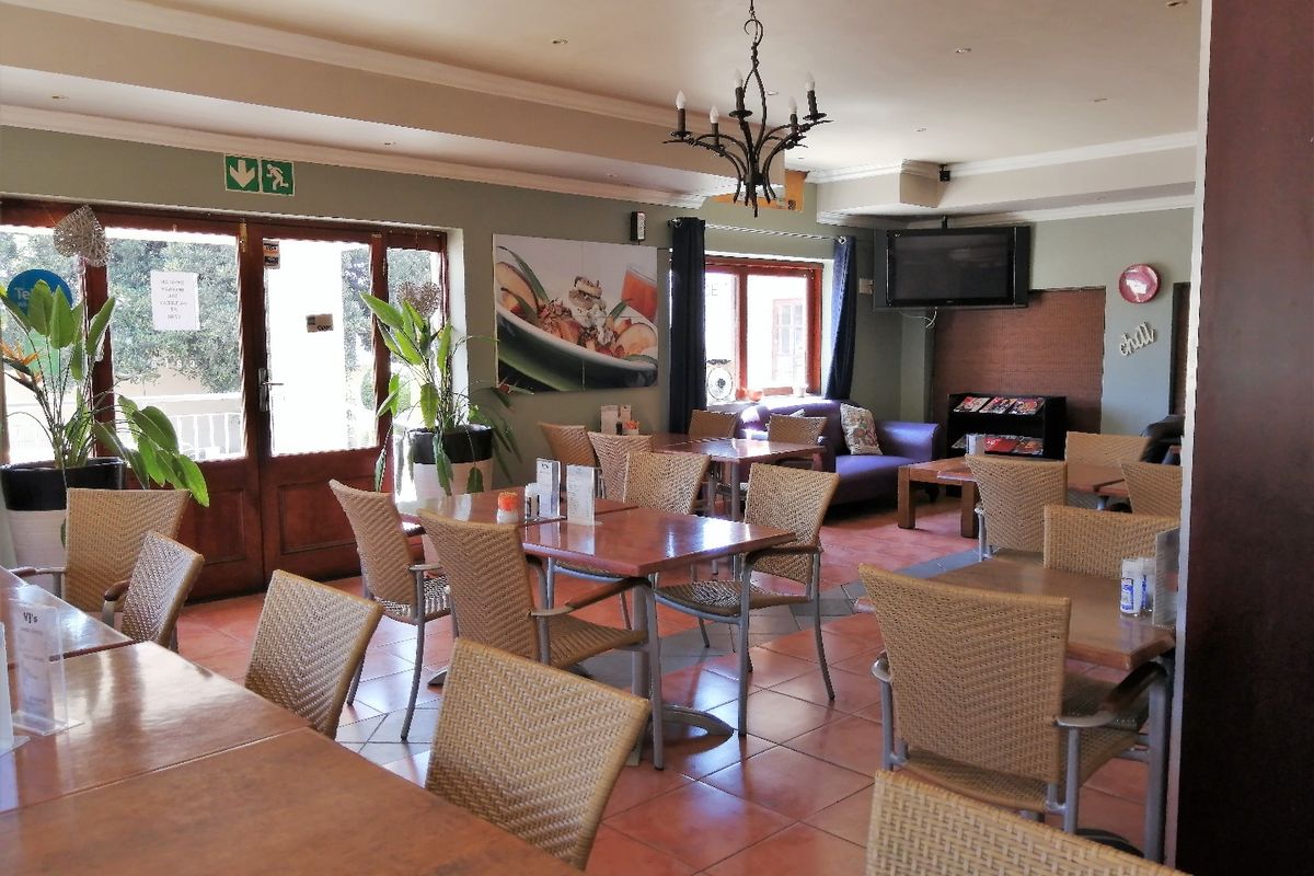 A spacious hotel lounge area featuring terracotta flooring, recessed lighting, and a decorative chandelier, providing a functional and welcoming communal space for guests.