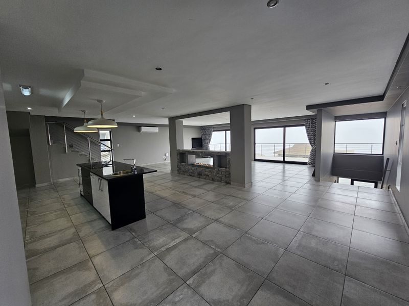 Spacious open-plan living area featuring a modern kitchen island, built-in fireplace, large sliding doors, and neutral tiled flooring throughout.