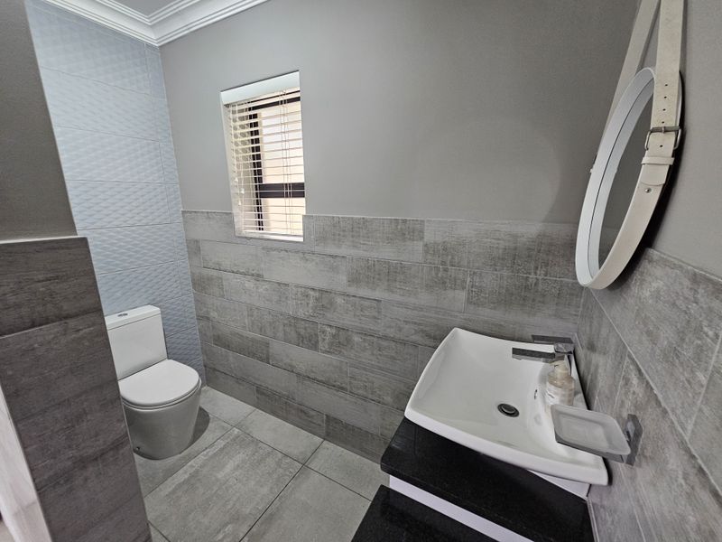 Modern bathroom featuring contemporary grey wall and floor tiles, a sleek vanity with basin, and a clean, minimalist aesthetic.