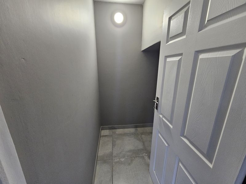 A small, clean utility or storage space featuring neutral grey walls, tiled flooring, and a single ceiling light fixture.