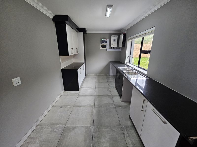 A clean, modern kitchen featuring granite countertops, ample built-in cabinetry, a double bowl sink, and integrated solar power infrastructure.