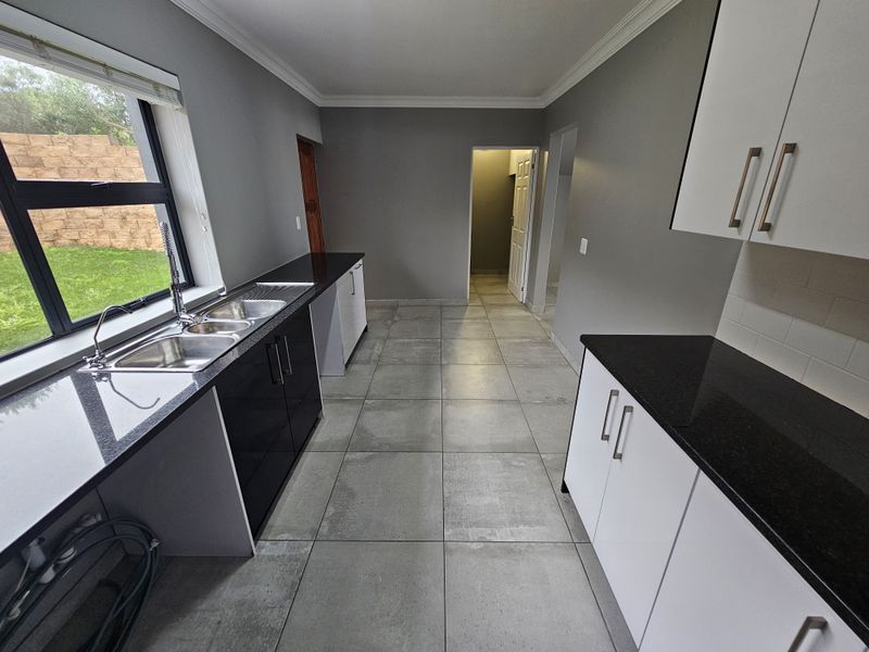 A clean, modern kitchen featuring contrasting black and white cabinetry, granite countertops, a double sink, and large format floor tiles.