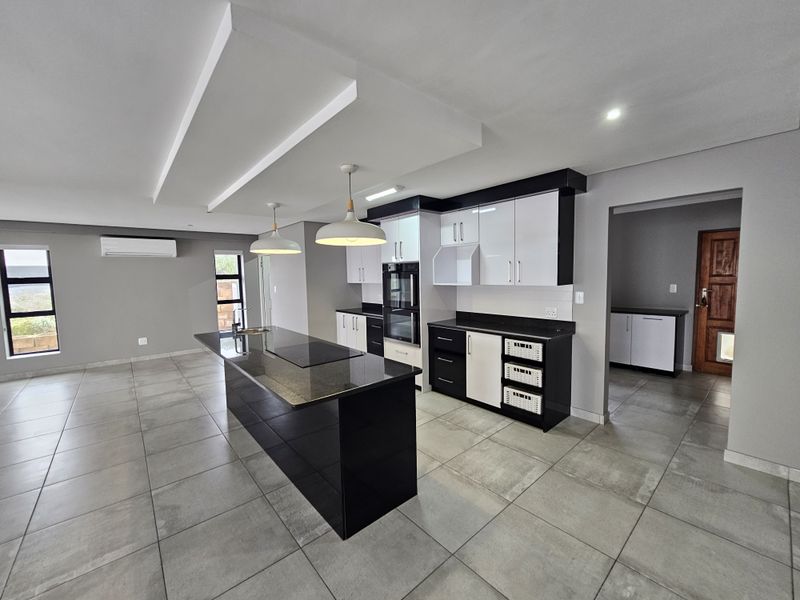 Modern open-plan kitchen featuring a central island, sleek black and white cabinetry, stone countertops, and integrated appliances, set within a spacious tiled living area.