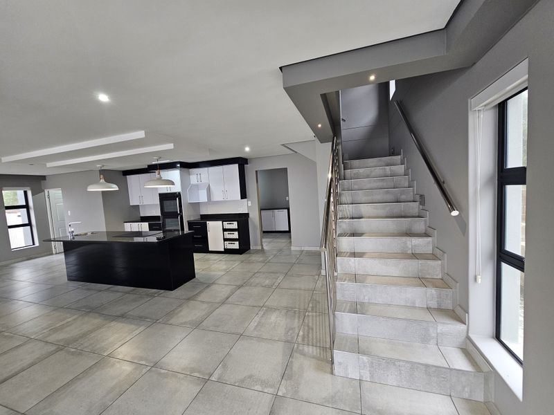 Spacious open-plan living area featuring a modern kitchen with a central island, sleek cabinetry, and a tiled staircase with a stainless steel handrail.