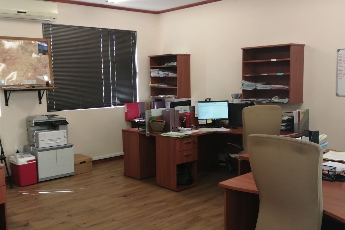 A functional office space featuring laminate flooring, wall-mounted shelving, and window blinds, providing a practical work environment.