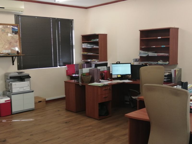 A functional office space featuring laminate flooring, wall-mounted shelving, and window blinds, providing a practical work environment.