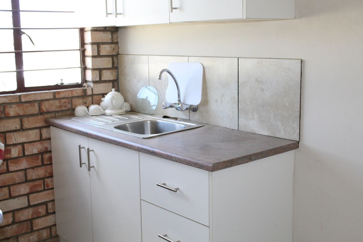 Compact kitchen area featuring built-in cabinetry, a stainless steel sink, tiled backsplash, and an exposed brick wall finish.
