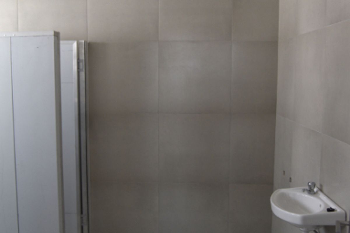A functional office restroom featuring large format wall and floor tiles, a wall-mounted basin, and a partition cubicle.